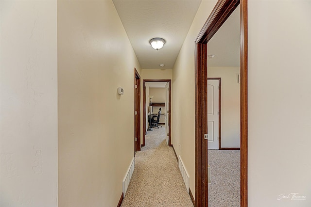 corridor with baseboards, a textured ceiling, visible vents, and light colored carpet