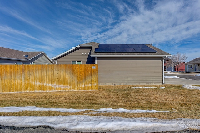 view of side of home with roof mounted solar panels, fence, and roof with shingles