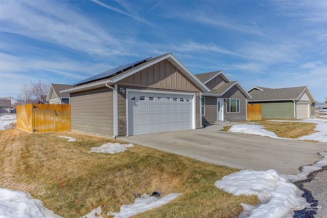 view of front of house with solar panels, concrete driveway, board and batten siding, fence, and a garage