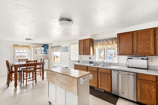 kitchen with brown cabinetry, dishwasher, a center island, light countertops, and a sink