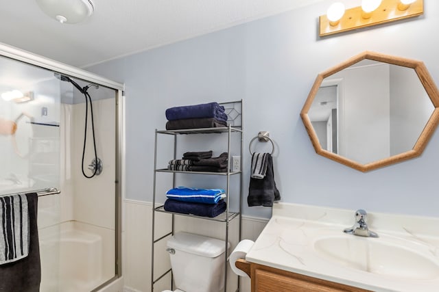 bathroom featuring toilet, a wainscoted wall, a shower stall, and vanity