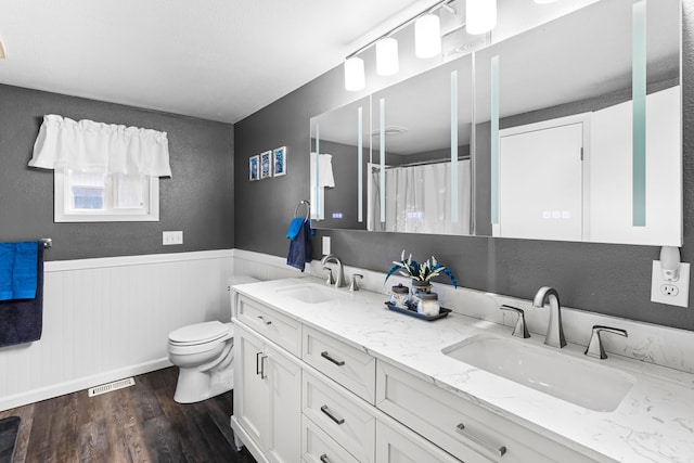 full bathroom with a wainscoted wall, a sink, visible vents, and wood finished floors