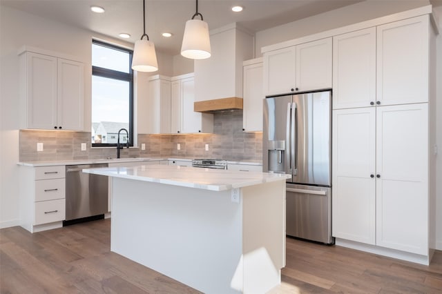 kitchen with stainless steel appliances, a kitchen island, a sink, white cabinets, and custom range hood