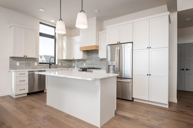 kitchen featuring a center island, stainless steel appliances, white cabinets, a sink, and wood finished floors