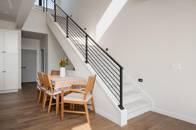 dining space with a towering ceiling, stairs, baseboards, and wood finished floors