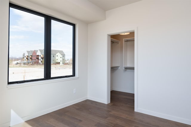 unfurnished bedroom featuring a closet, dark wood finished floors, a spacious closet, and baseboards