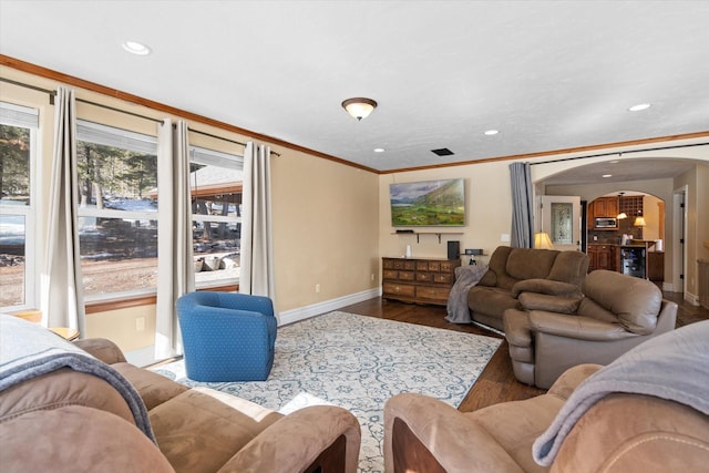 living area featuring arched walkways, ornamental molding, plenty of natural light, and wood finished floors