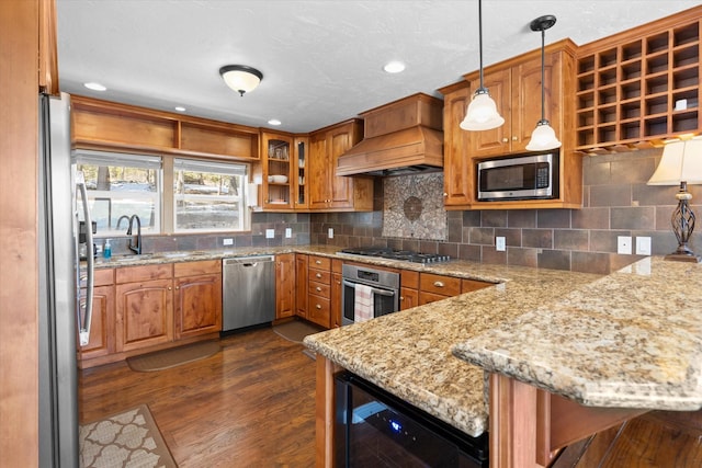 kitchen featuring brown cabinetry, wine cooler, appliances with stainless steel finishes, a peninsula, and premium range hood