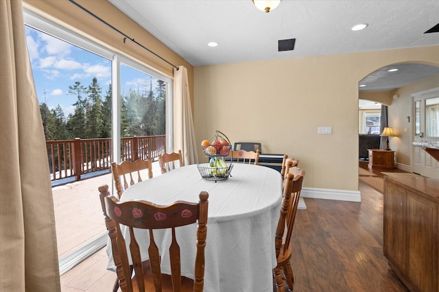 dining space featuring baseboards, arched walkways, wood finished floors, and recessed lighting