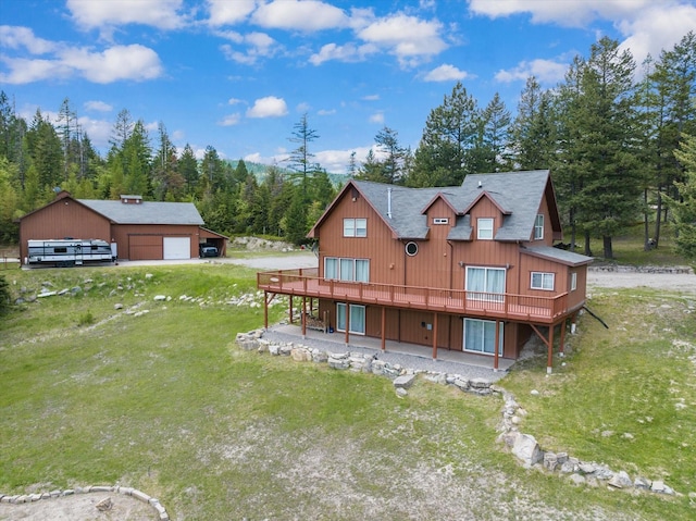 rear view of property with a lawn, a garage, an outdoor structure, driveway, and a wooden deck