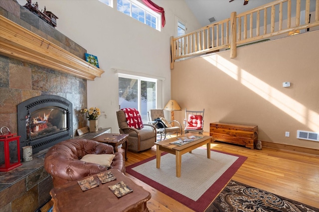 living area with a high ceiling, visible vents, a tiled fireplace, and wood finished floors