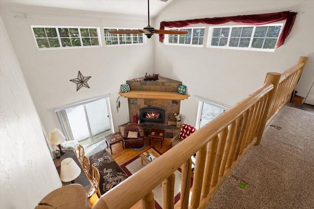 living area featuring a warm lit fireplace, a ceiling fan, vaulted ceiling, and wood finished floors