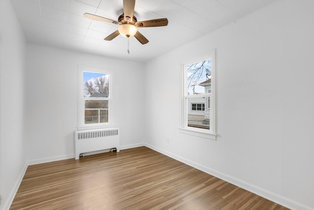 empty room with a healthy amount of sunlight, wood finished floors, and radiator