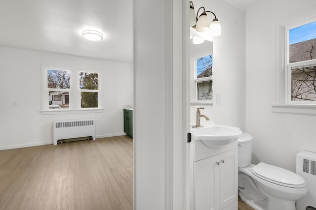 half bath featuring a healthy amount of sunlight, toilet, vanity, and radiator heating unit