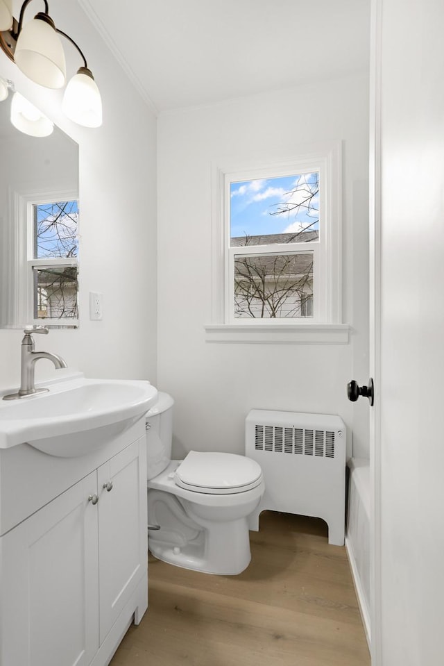 bathroom with a wealth of natural light, radiator, toilet, and wood finished floors