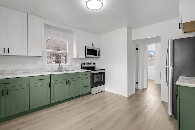 kitchen featuring stainless steel appliances, a sink, white cabinetry, green cabinets, and light wood finished floors