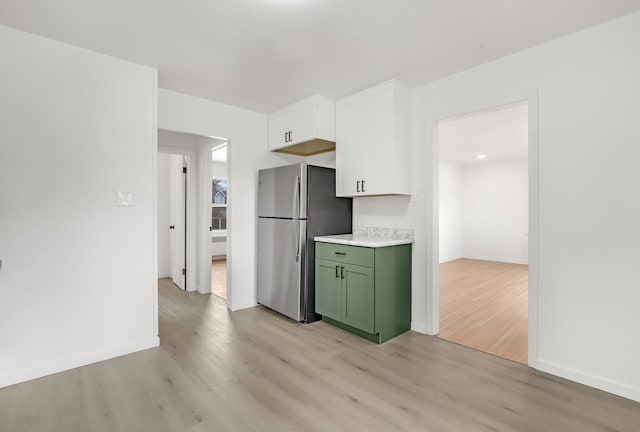 kitchen with light countertops, green cabinets, light wood-style floors, freestanding refrigerator, and white cabinets