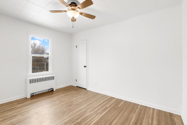 spare room featuring light wood finished floors, radiator heating unit, baseboards, and a ceiling fan