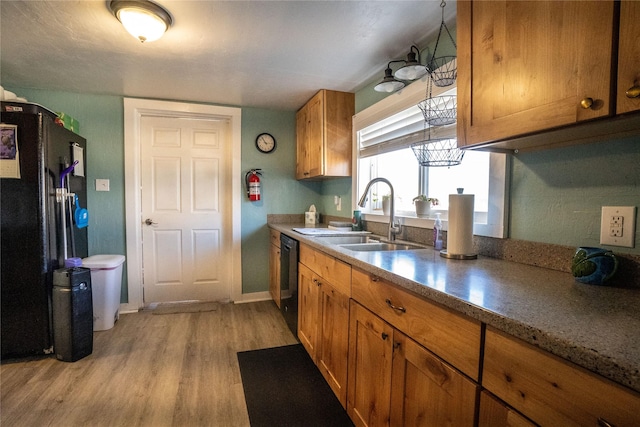 kitchen featuring light wood finished floors, baseboards, brown cabinetry, black appliances, and a sink