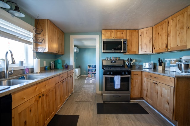 kitchen with stainless steel appliances, a wall mounted AC, a sink, wood finished floors, and baseboards