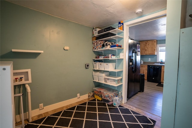 interior space featuring light wood finished floors, black fridge with ice dispenser, and baseboards