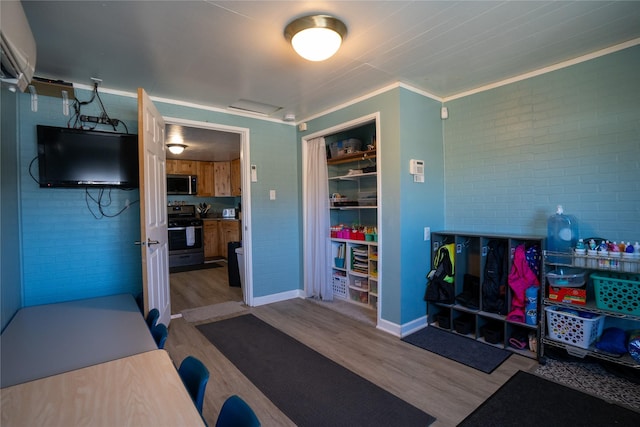 workout room with ornamental molding, baseboards, brick wall, and wood finished floors