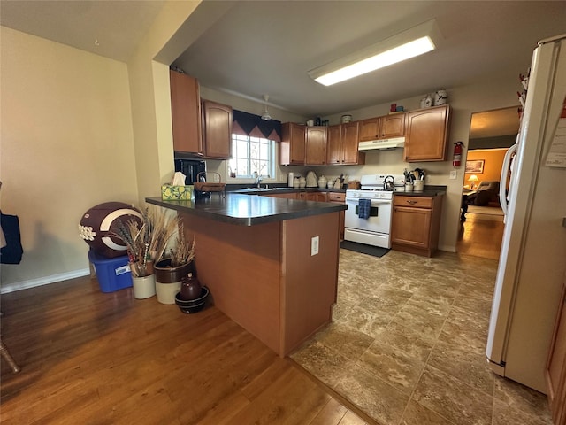 kitchen with dark countertops, white appliances, under cabinet range hood, and a peninsula