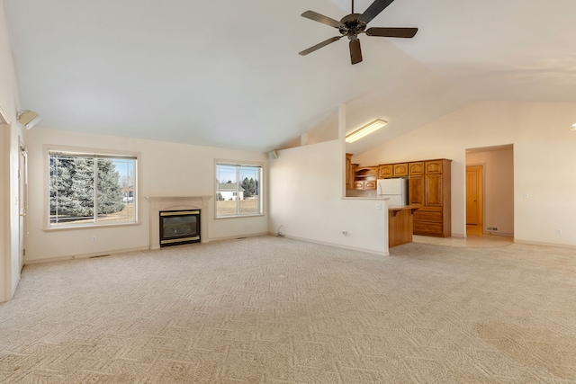 unfurnished living room with high vaulted ceiling, light carpet, a ceiling fan, baseboards, and a glass covered fireplace