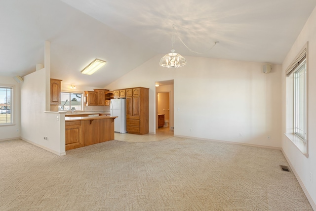 kitchen featuring visible vents, brown cabinetry, light colored carpet, freestanding refrigerator, and a peninsula