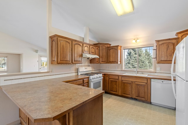 kitchen featuring white appliances, a peninsula, vaulted ceiling, light floors, and a sink