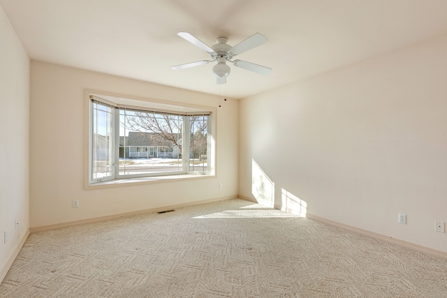 empty room featuring carpet floors, visible vents, ceiling fan, and baseboards