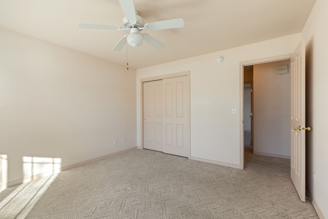 unfurnished bedroom featuring a ceiling fan, a closet, light carpet, and baseboards