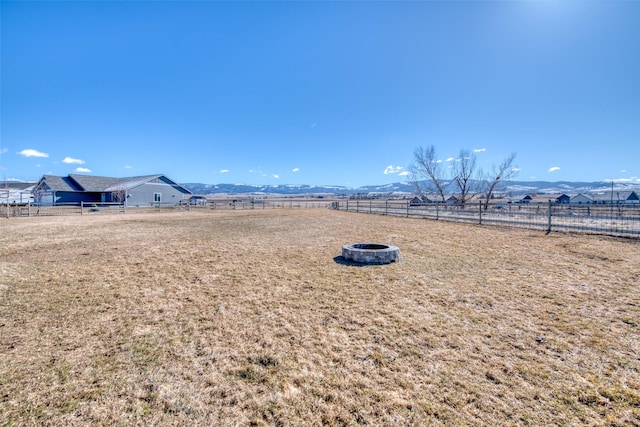 view of yard featuring an outdoor fire pit, a rural view, fence, and a mountain view