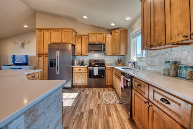 kitchen with light countertops, light wood-style flooring, appliances with stainless steel finishes, vaulted ceiling, and a sink