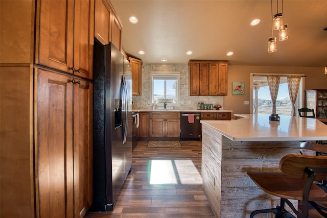 kitchen with stainless steel fridge with ice dispenser, dishwashing machine, brown cabinets, light countertops, and a kitchen bar