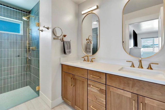 full bathroom featuring a tile shower, double vanity, a sink, and baseboards