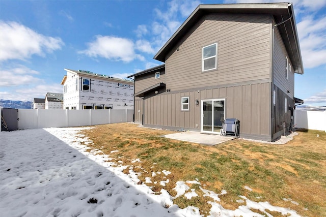 snow covered rear of property featuring a patio, a lawn, and fence