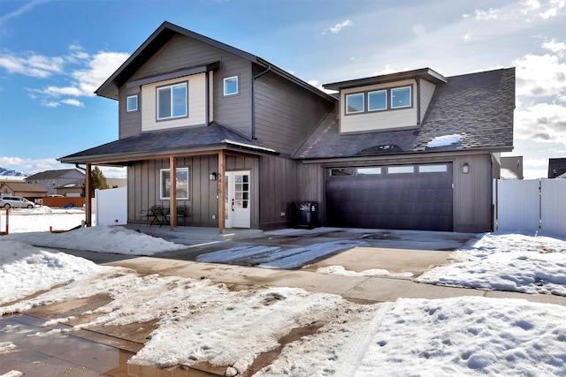 view of front of house featuring a shingled roof, an attached garage, board and batten siding, fence, and driveway