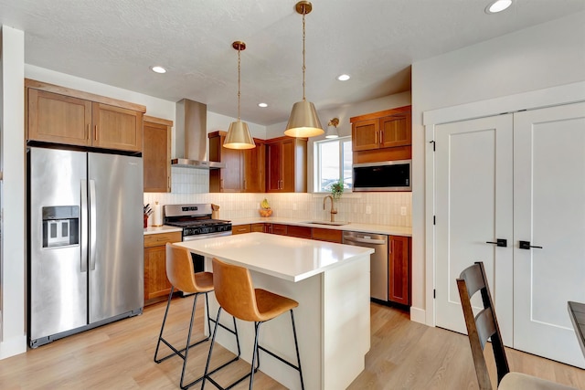 kitchen with stainless steel appliances, wall chimney range hood, a sink, and light wood-style floors