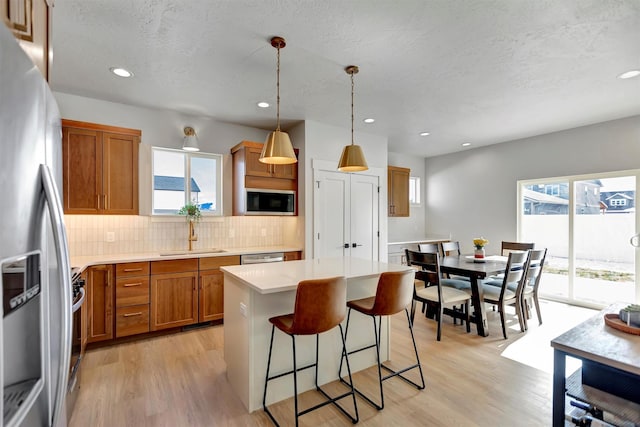 kitchen featuring stainless steel appliances, tasteful backsplash, brown cabinetry, a sink, and a kitchen breakfast bar