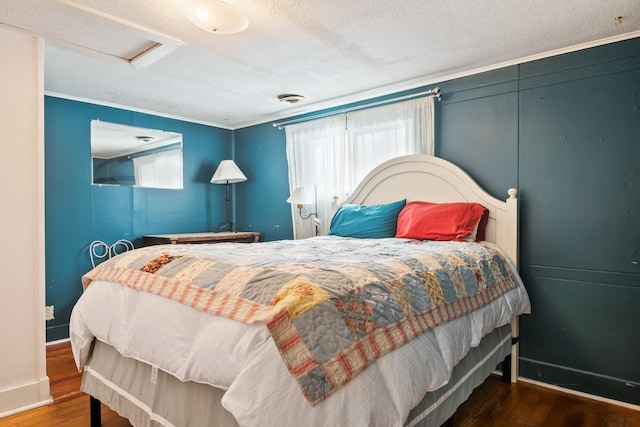 bedroom with attic access, a textured ceiling, baseboards, and wood finished floors