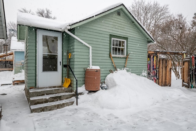 snow covered rear of property featuring entry steps and fence