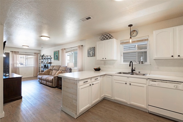 kitchen featuring white dishwasher, a peninsula, wood finished floors, a sink, and white cabinetry