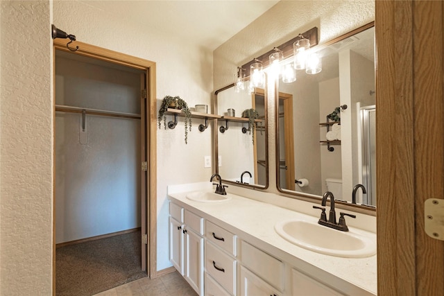 full bath featuring double vanity, a sink, toilet, and a shower with door