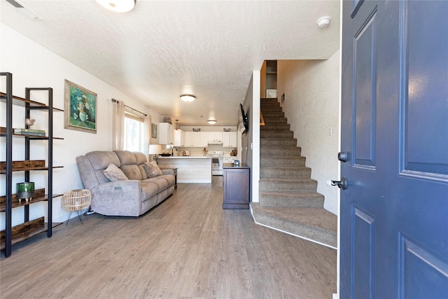 living area with stairs, visible vents, a textured ceiling, and light wood-style flooring