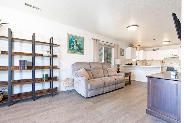 living area featuring light wood-style floors, visible vents, and a textured ceiling