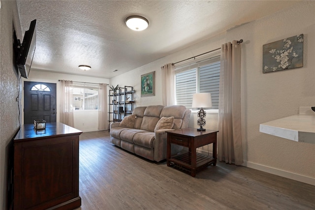 living room featuring a textured ceiling, a textured wall, wood finished floors, and baseboards