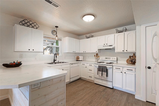 kitchen with under cabinet range hood, a peninsula, white appliances, a sink, and visible vents