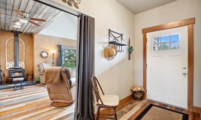 entryway with a wood stove, wood finished floors, a ceiling fan, baseboards, and lofted ceiling