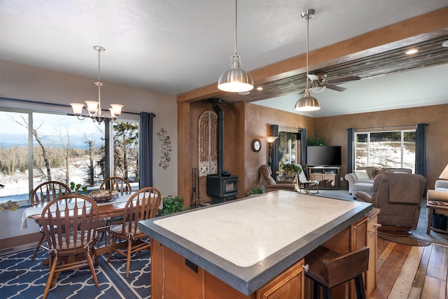 kitchen featuring beam ceiling, open floor plan, dark wood finished floors, brown cabinetry, and a wood stove